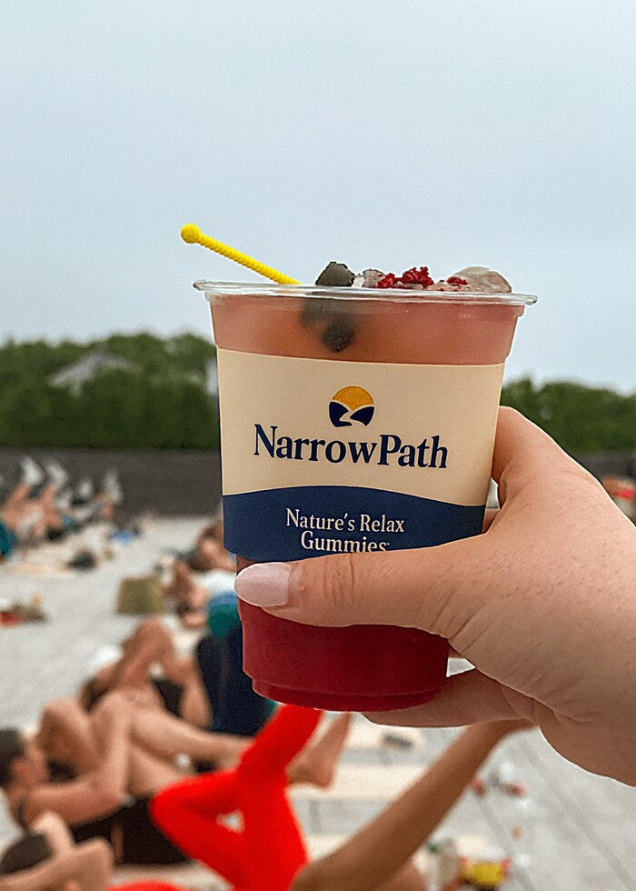 A NarrowPath Natures Relax Gummies smoothie cup held up on a sunny beach
