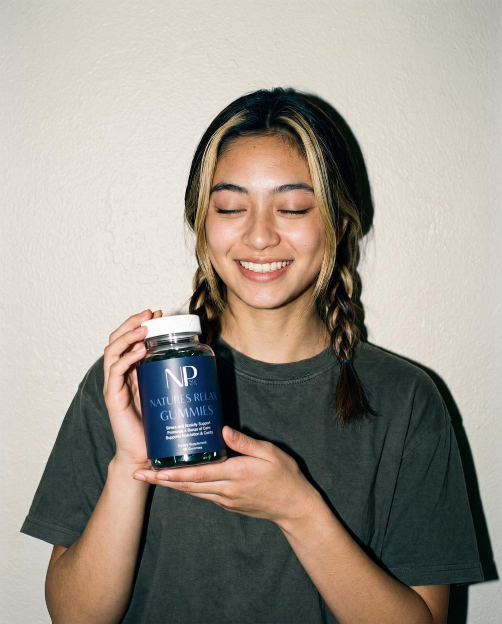A smiling woman with braids holding two dark green Natures Relax gummies and the bottle