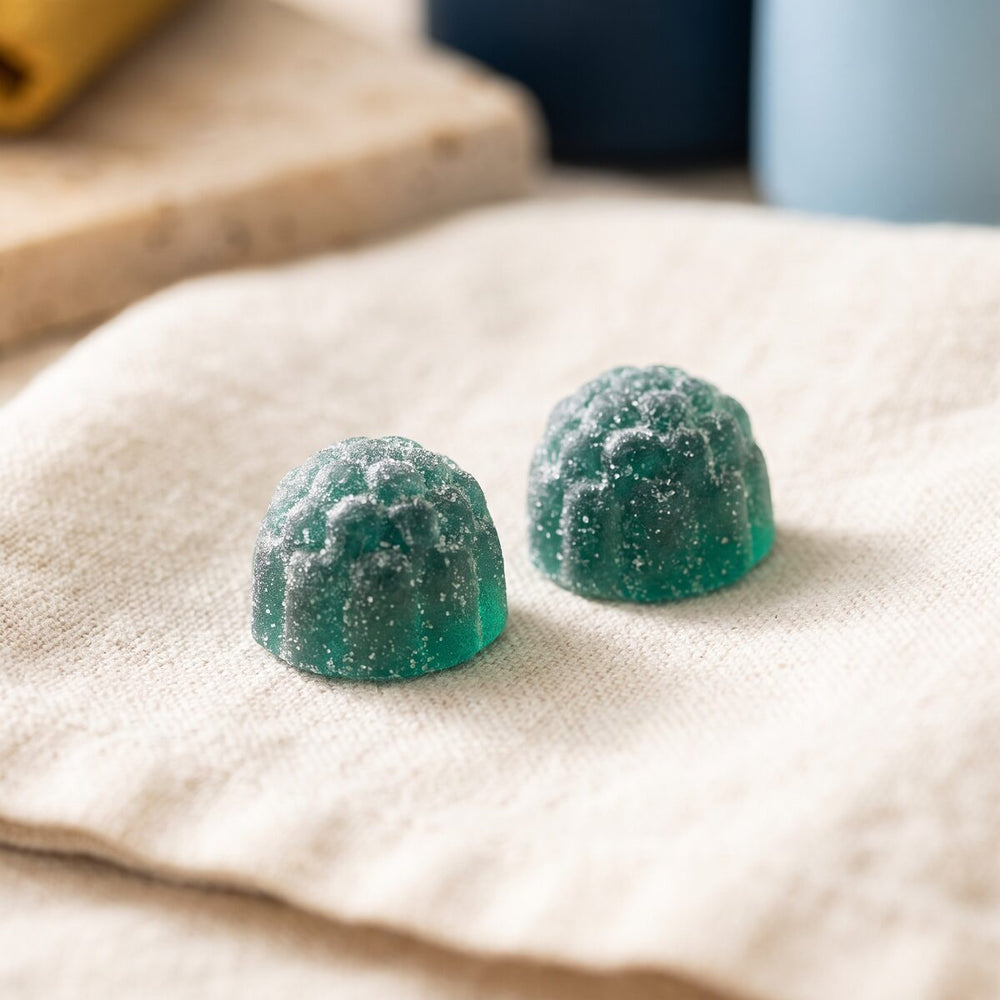 Macro photograph of two teal, sugar-dusted Natures Relax berry-shaped gummies on linen