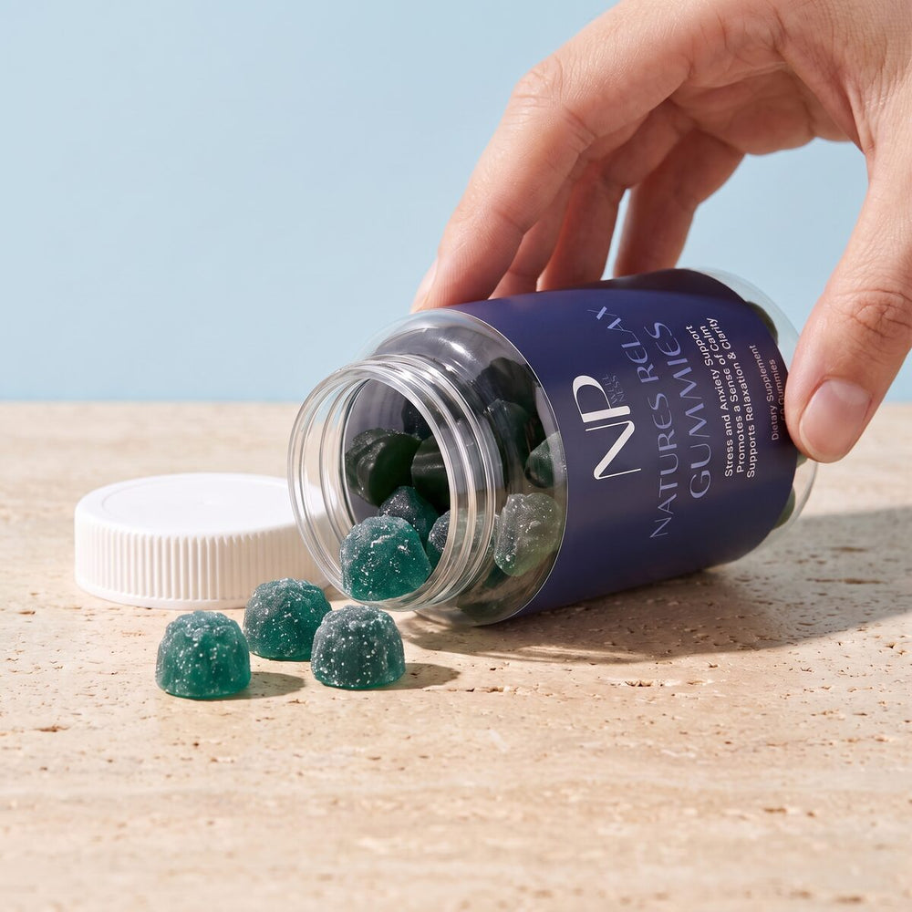 An open jar of Natures Relax Gummies tipped on travertine with teal berry-shaped gummies spilling out