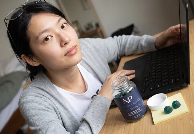 A woman relaxing at her home desk mid afternoon, a bottle of Natures Relax Gummies beside her laptop and coffee