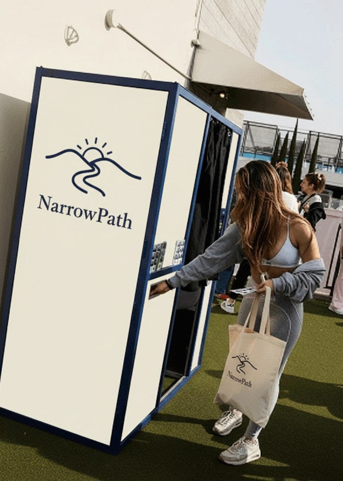 A woman stepping into a NarrowPath photo booth at an outdoor event, tote bag in hand